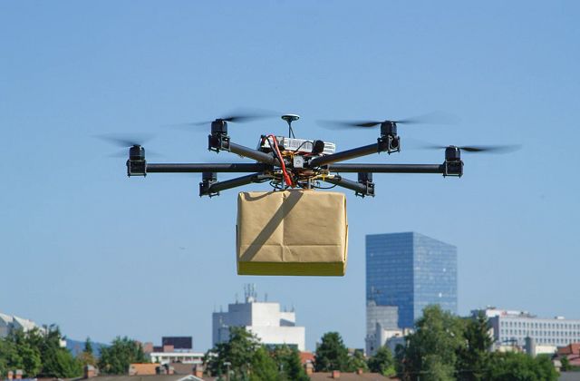 A drone flying outdoors carrying a package wrapped in plain brown paper