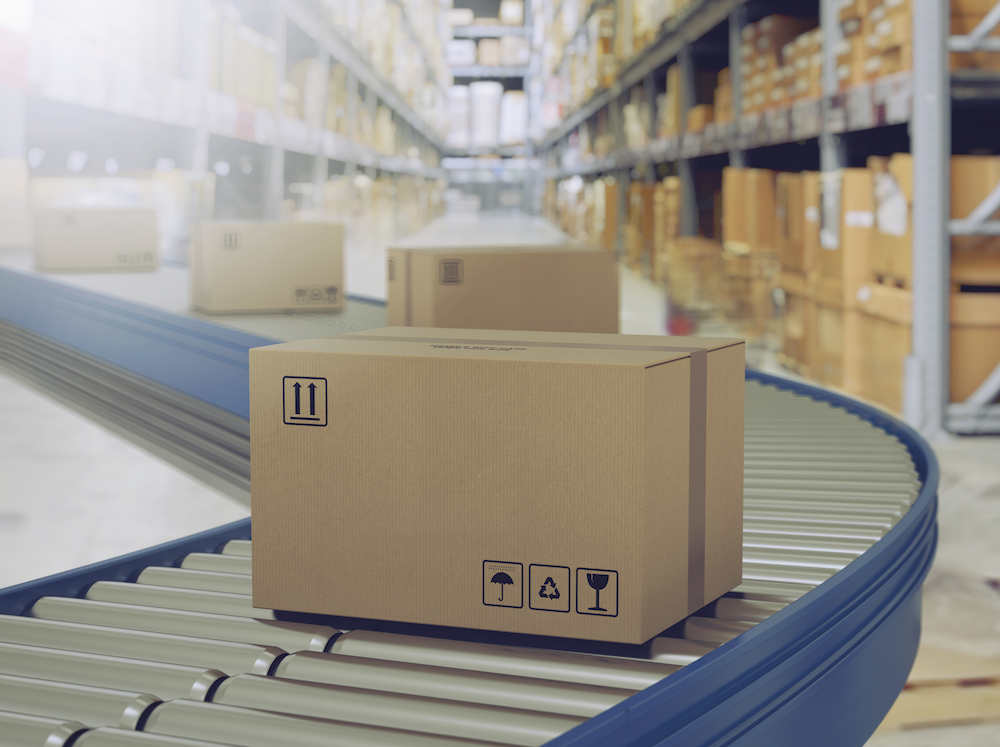 Cardboard boxes traveling down a conveyor system, with racks of boxes in the background